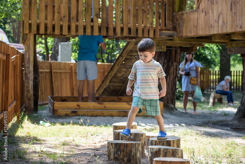 Little boy climbing on a wooden playground in rope park. Kid play outdoors warm sunny summer day