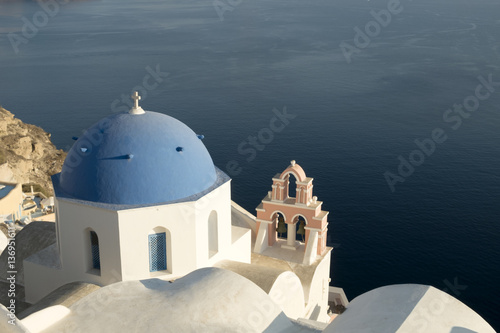 A famous blue domed church at Oia village, Santorini with the volcano's caldera in the background