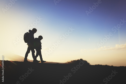 Silhouettes of father and son hiking at sunset
