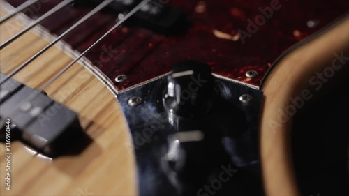Vintage bass guitar in light wooden color. With red pickguard and two single pickups. Silver bridge. Close-up smooth motion.