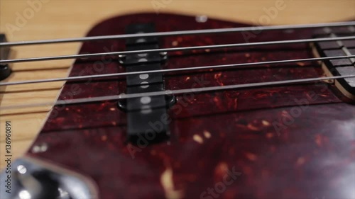 Vintage bass guitar in light wooden color. With red pickguard and two single pickups. Silver bridge. Close-up smooth motion.