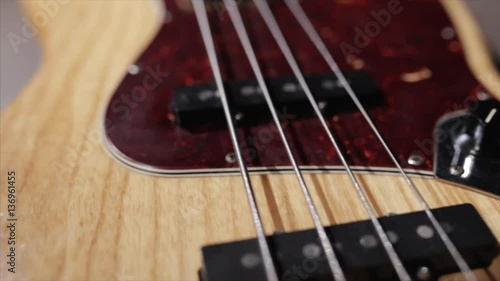 Vintage bass guitar in light wooden color. With red pickguard and two single pickups. Silver bridge. Close-up smooth motion.