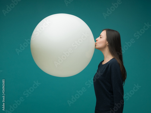 funny young woman with long dark hair inflating huge balloon on blue background photo