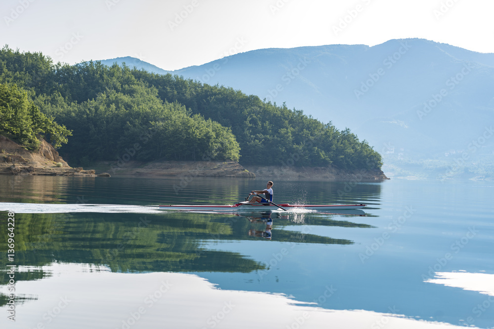 Fototapeta premium A Young single scull rowing competitor paddles on the tranquil lake
