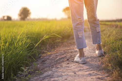 Closeup picture of legs of beautiful woman (lonely girl),wearing white sneakers and blue jeans. Walk on the pathway and green fields beside, Ayutthaya, central of Thailand.