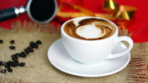 Cappuccino coffee and gold ribbons. A cup of latte  cappuccino or espresso coffee with milk on red background with dark roasting coffee beans. Drawing the foam milk on top.