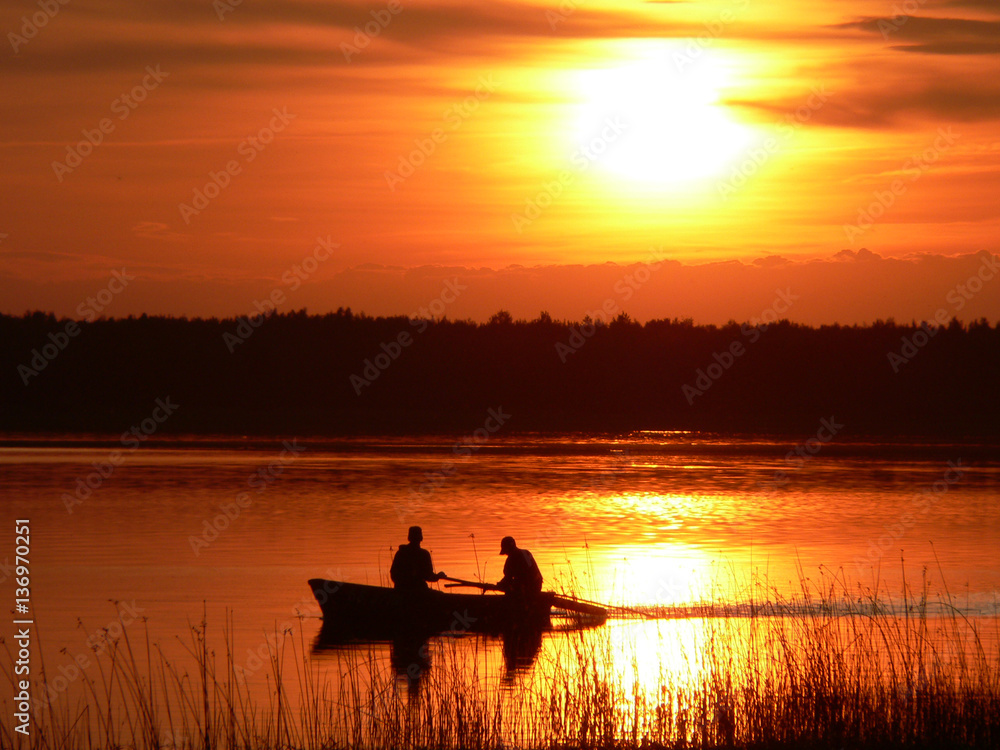 Bright orange sunset on the lake. Fishermen catch fish