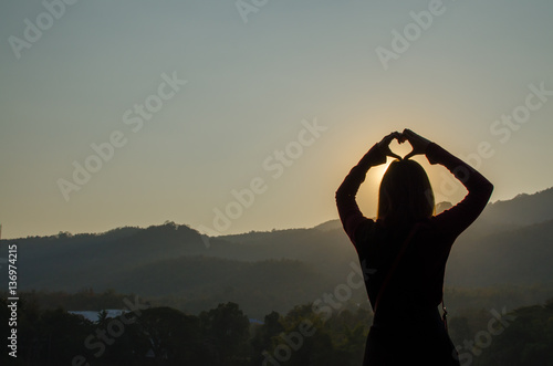 Silhouette of Asia Woman making Sign of Heart with the Sunlight when Sunset.