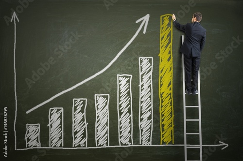 Successful businessman is standing on ladder and drawing growing graph of profit on blackboard. Investment concept. photo