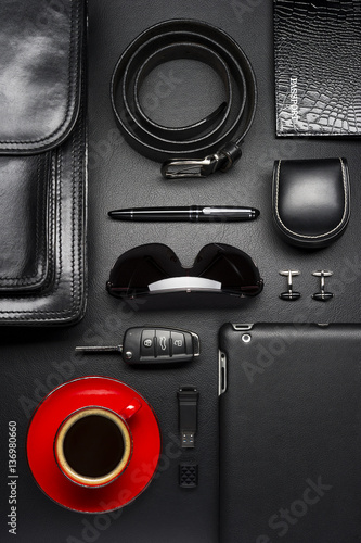 Man accessories in business style with cup of coffee, gadgets, car key, cufflinks, sunglasses, briefcase and other luxury businessman attributes on leather black background, fashion industry