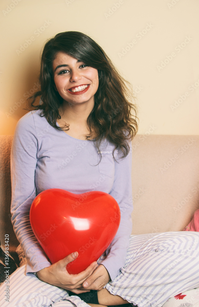 Preciosa y sonriente chica joven en pijama sujetando un globo con forma de corazón Preciosa y sonriente chica joven en pijama sujetando un globo con forma de corazón