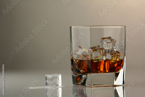 A glass of whiskey on a glass table with a cube of melting ice