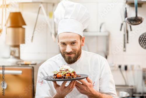 Portrait of chef cook in uniform standing with delicious dish at the kitchen photo