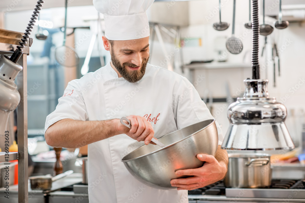 Chef cook in uniform mixing salad in the metal vessel at the restaurant kitchen Chef cook in uniform mixing salad in the metal vessel at the restaurant kitchen