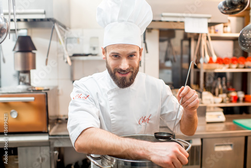 Portrait of a chef cook in uniform with big cooker at the restaurant kitchen