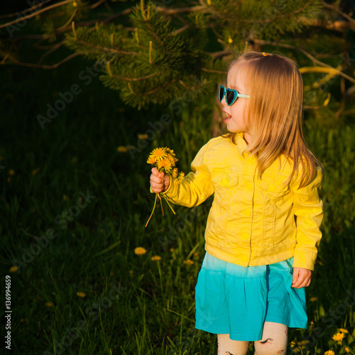 Trendy little girl with dandelions in the evening sun