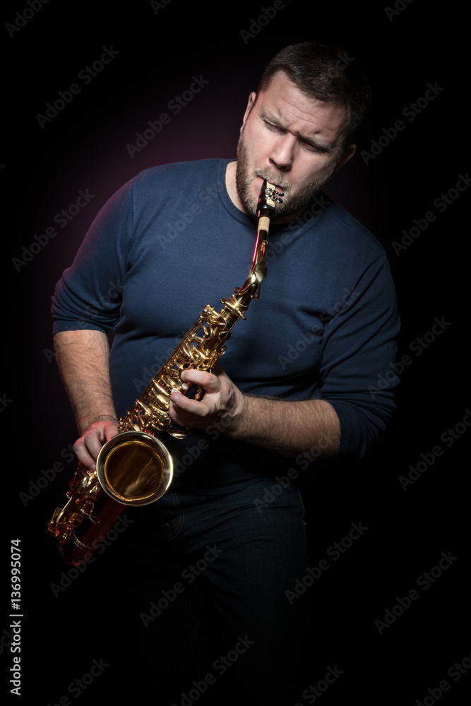Naklejka premium Bearded saxophonist with closed eyes hysterically plays a saxophone, isolated on a black background