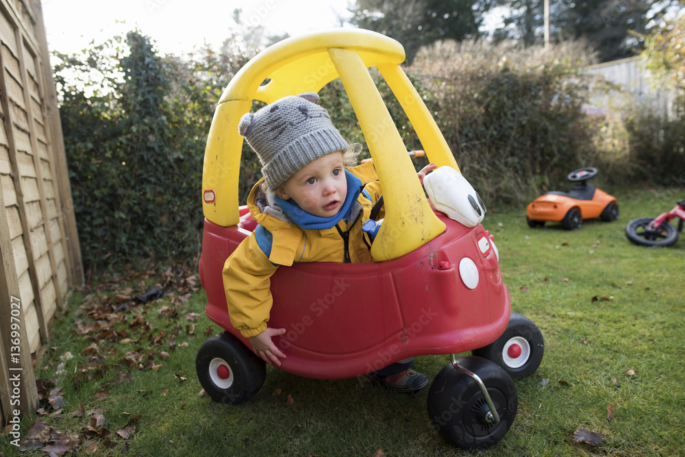 Girl driving toy car in backyard Girl driving toy car in backyard