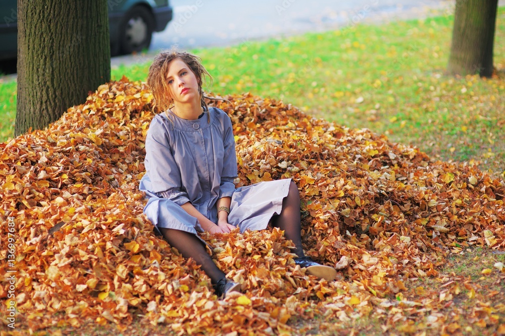 Portrait of pretty tired girl in a purple cloak, resting on yellow autumn leaves. Portrait of pretty tired girl in a purple cloak, resting on yellow autumn leaves.