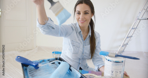 Smiling young woman checking out a blue paint color that she has mixed on her brush while preparing to repaint and redecorate her apartment