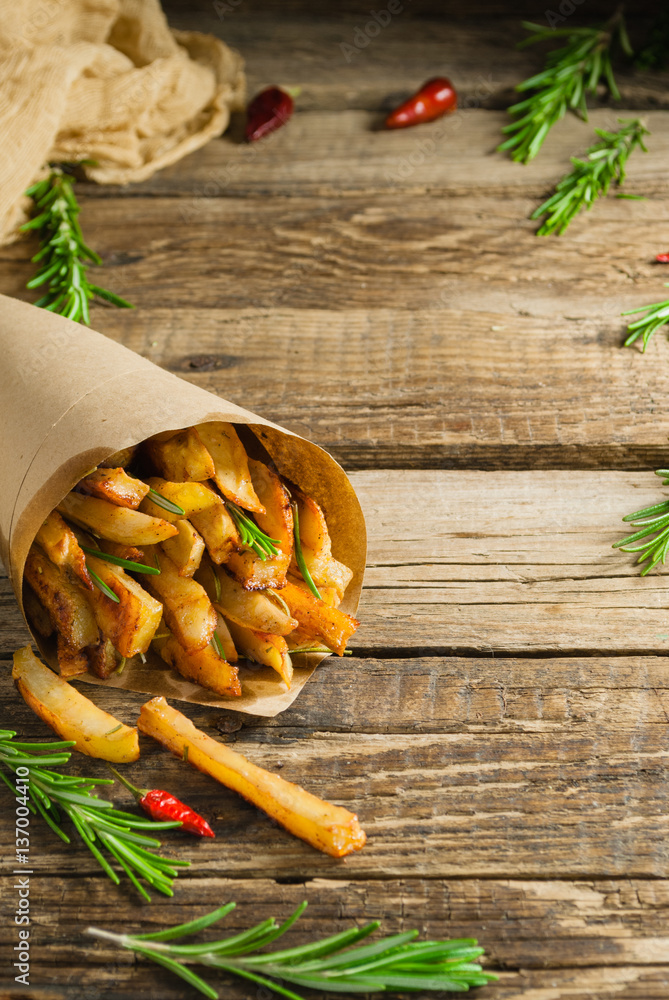 French fries potatoes with rosemary in paper bag over old wooden