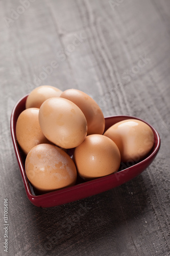 Brown Colored Eggs in red heart-shaped bowl on dark wood background