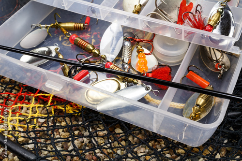 Open storage box with accessories for fishing and fishing baits on the stony ground