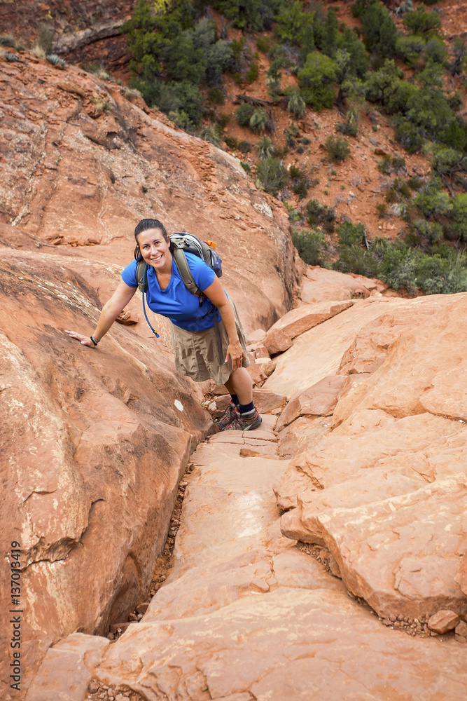 Female hiker climbing a steep red rock cliff