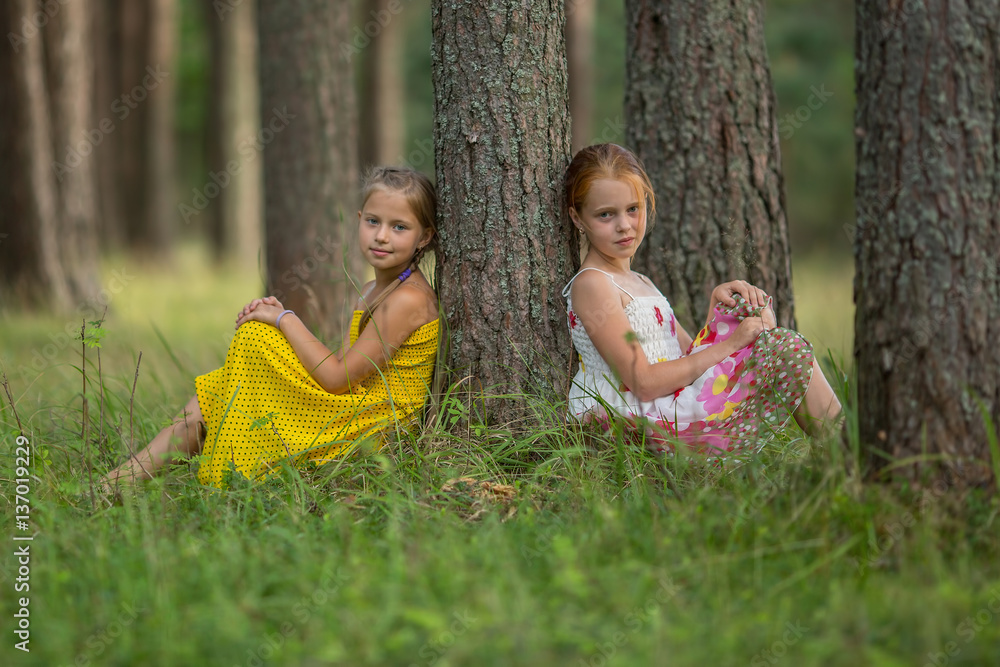 Φωτογραφία Little sisters are sitting near a tree in the Park.
