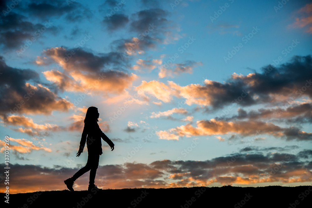 Silhouette woman walking at sunset.