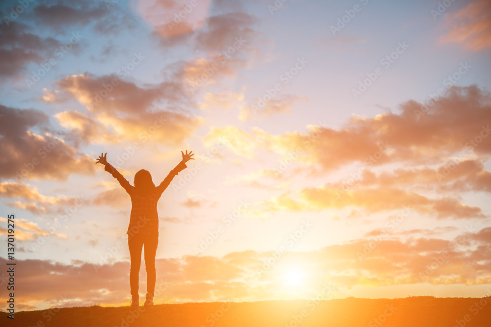 Silhouette woman at sunset standing elated with arms raised up.