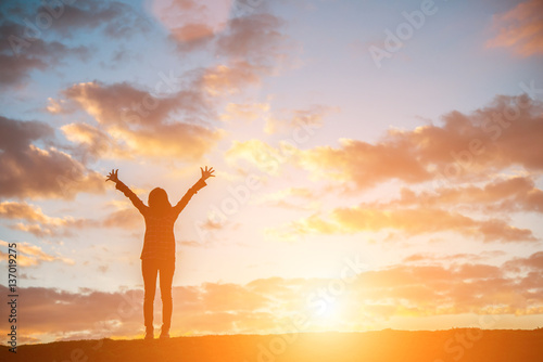Silhouette woman at sunset standing elated with arms raised up. photo