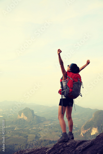 Cheering young woman hiker at mountain top