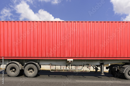 The close-up of red container on the truck at the hi-way with the sky.The side of the container.