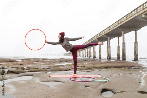 Girl in a red hat, red leggings and a gray sweater practicing yoga near a pier on a cloudy day. California, San Diego, Ocean beach pier.  Hula hup photo