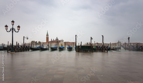 Gondolas by Saint Mark square during with San Giorgio di Maggiore church in the background in Venice Italy during high tide
