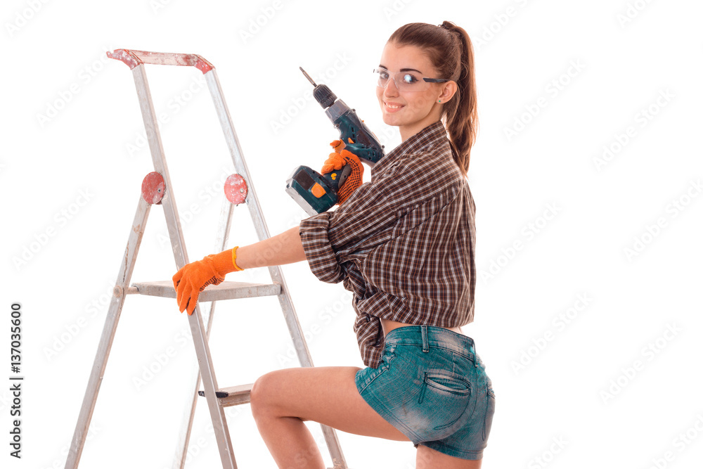 cheerful young brunette builder girl in uniform and glasses makes renovation with drill in her hands isolated on white background cheerful young brunette builder girl in uniform and glasses makes renovation with drill in her hands isolated on white background