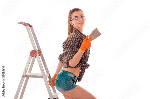 lovely young brunette builder girl in uniform and glasses makes renovation isolated on white background