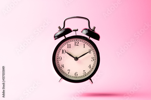 black vintage alarm clock floating on the air with pink color ba