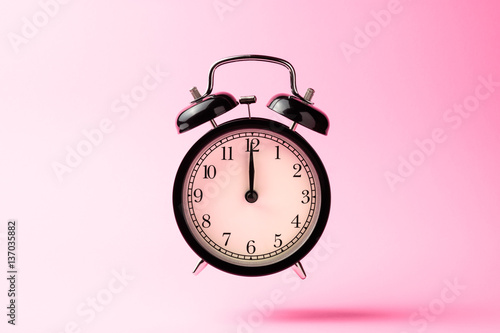 black vintage alarm clock floating on the air with pink color ba