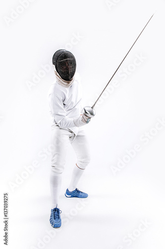 Man wearing fencing suit practicing with sword against gray