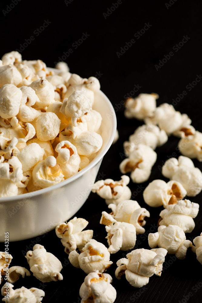 Popcorn in a white ceramic bowl on a black wooden table, selective focus, vertical Popcorn in a white ceramic bowl on a black wooden table, selective focus, vertical