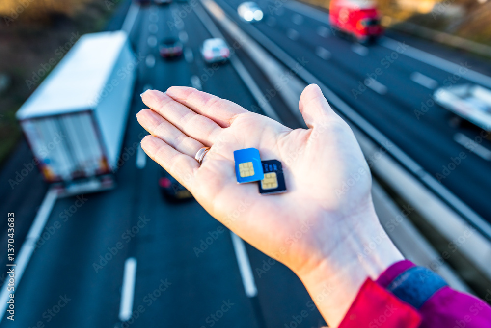 Day view of woman hand holding sim cards over UK Motorway.