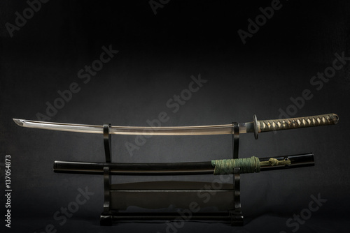 Japanese iaido sword in black wooden stand and black background. Still life studio shot with center light.  photo