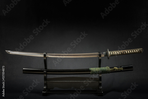 Japanese iaido sword in black wooden stand and black background. Still life studio shot with center light. 