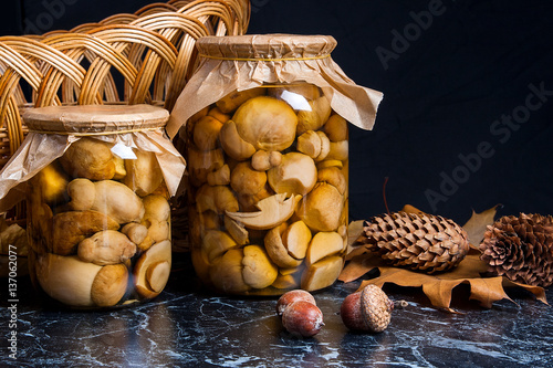 Two glass jars with wild marinated mushrooms on black marble bac
