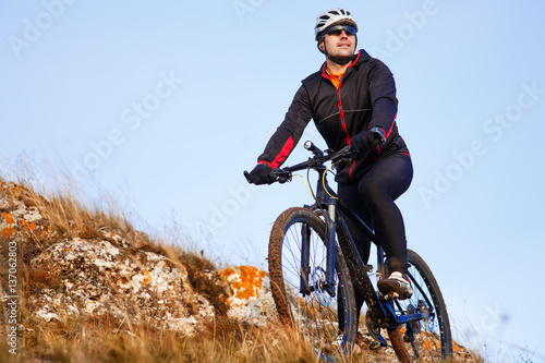 Mountain biker looking at inspiring mountain landscape, standing with bicycle.