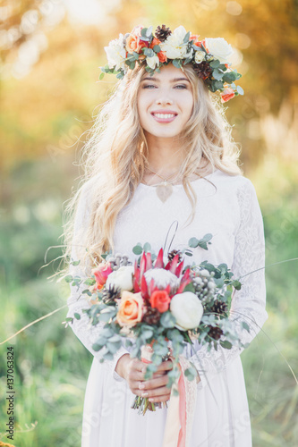 Beautiful blond bride with a wedding bouquet in rays of the sun. Summer wedding.