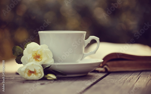 Old open book and a white cup with a wild roses