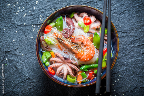 Hot seafood noodle in dark bowl with chopsticks